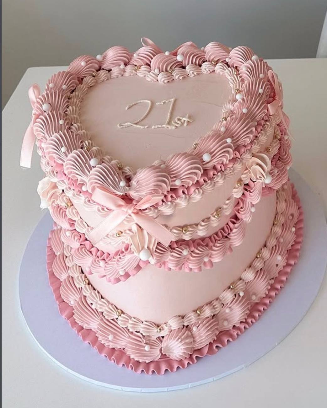 A pink two-tier heart cake for a 21st, piped by hand with shell borders, pearls and satin bows